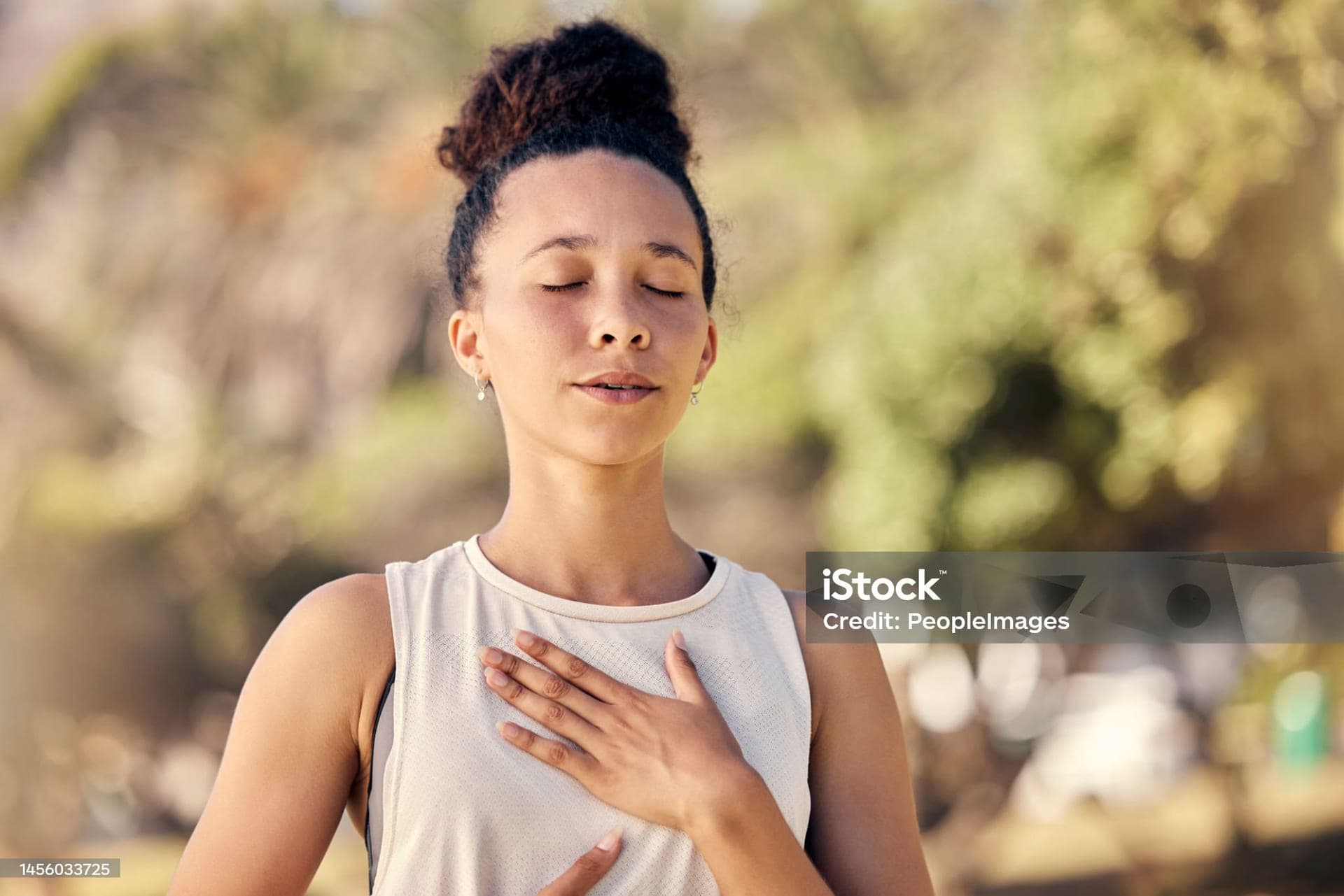 A woman breathing slowly outdoors, a hand on her chest