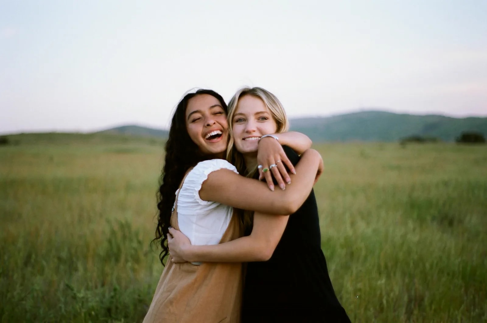Two young women hugging and laughing in a grassy field