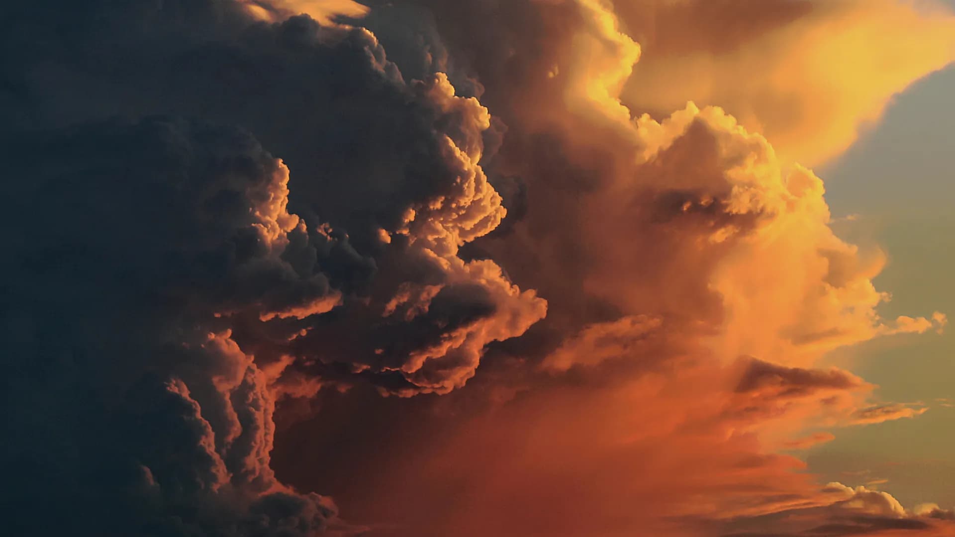 A storm cloud lit orange by low sun, against a clearing blue sky